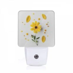 Night Light, A Yellow Flower With Yellow Petals And Green Leaves Is Placed On A White Surface.